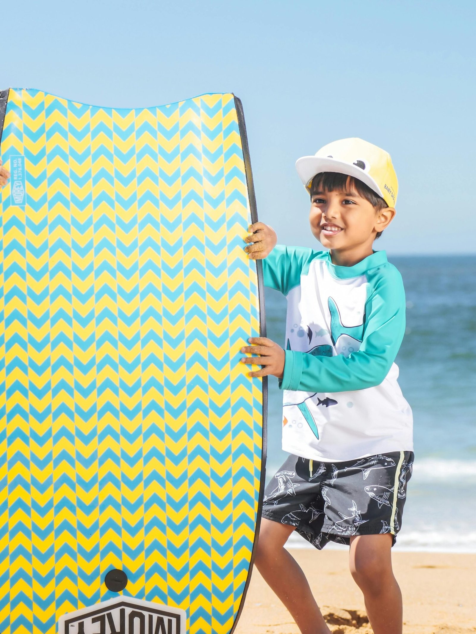 Cheerful boy enjoying a sunny day at the beach with his colorful bodyboard.